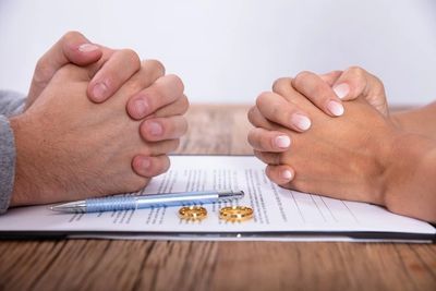 Hands folded over a document with wedding rings and pen.