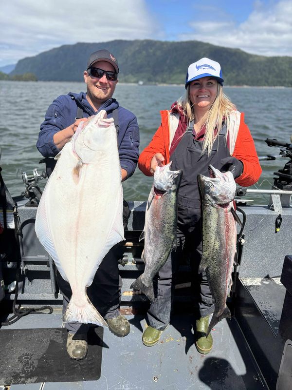 Two people on a boat holding large fish they caught.