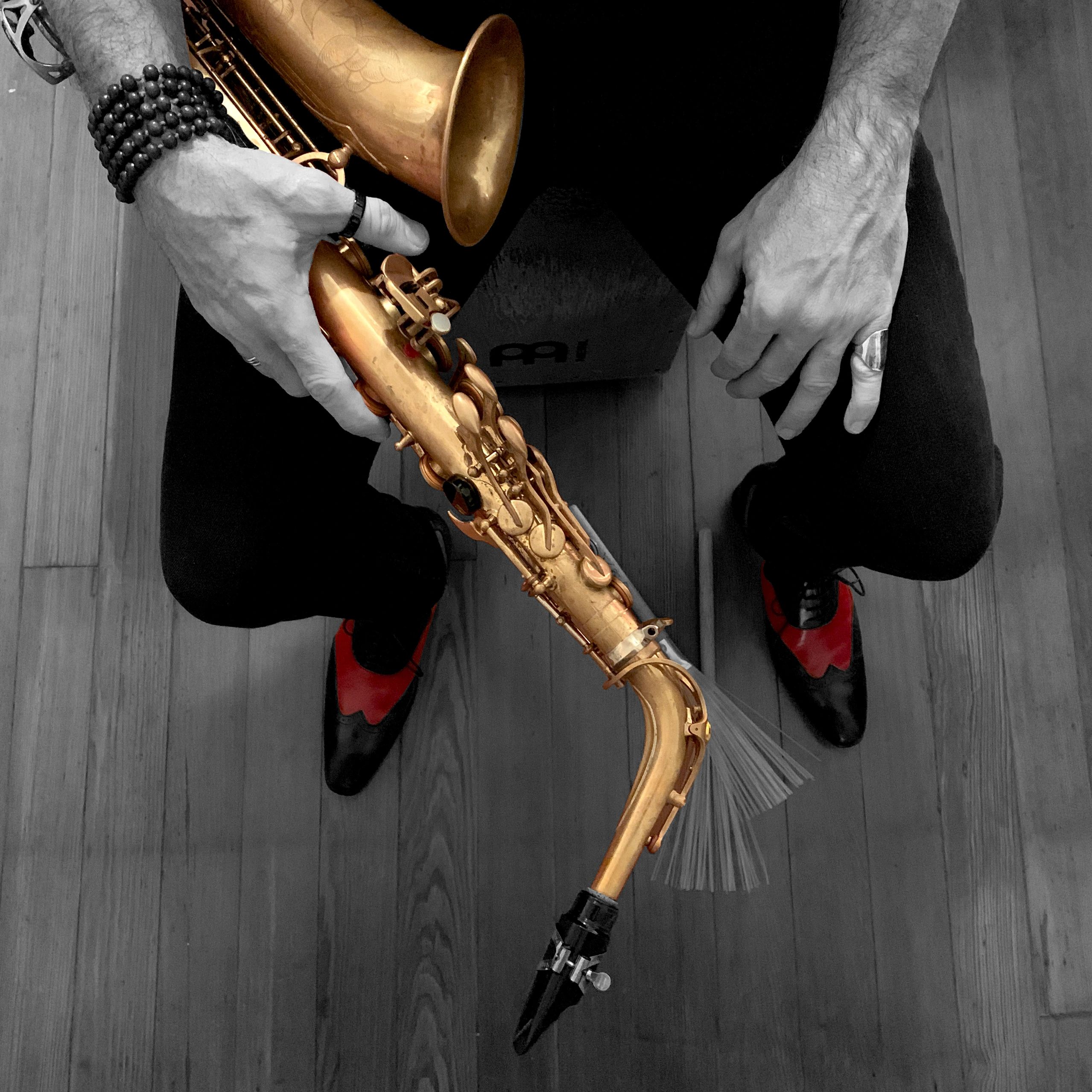 Person holding a golden saxophone, wearing beaded bracelets and red-black shoes.