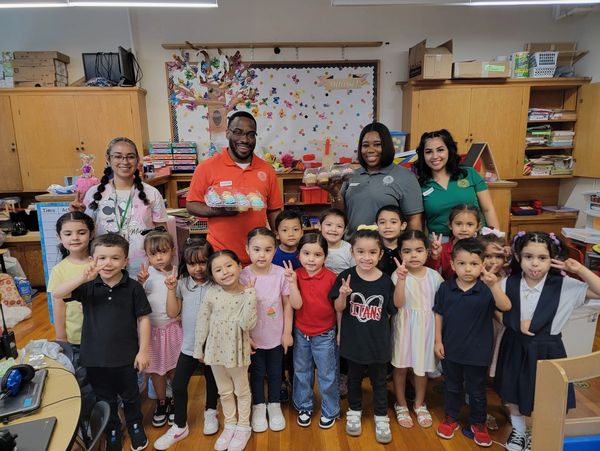 Group of children and adults posing happily in a classroom with cupcakes.