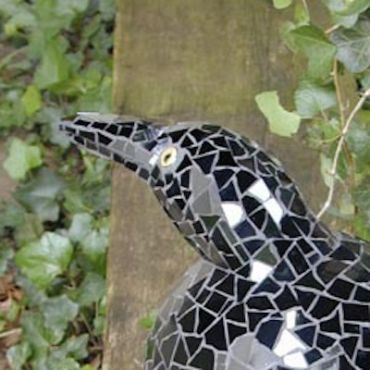 Black mosaic bird sculpture against a natural background.