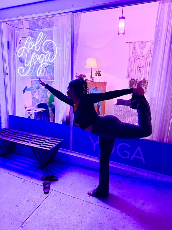 Person practicing yoga outside a studio with purple lighting.