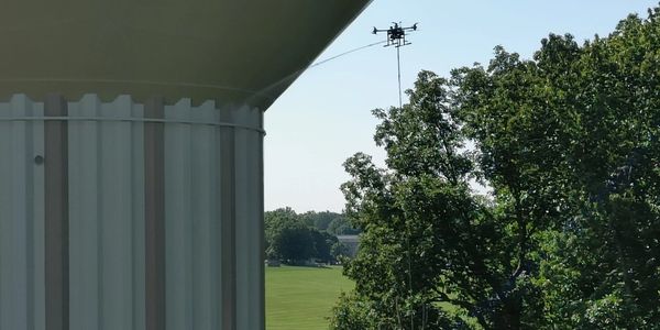 A drone pressure washing a water tower on bright sunny day