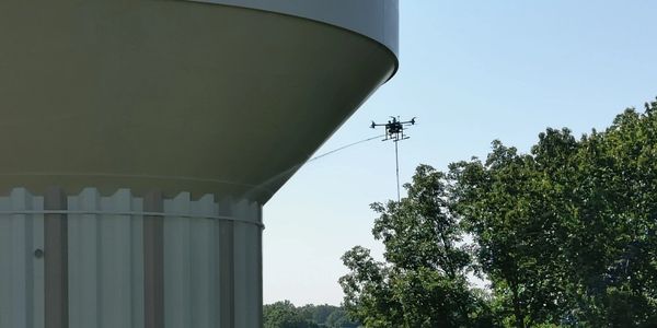 A drone pressure washing a water tower on bright sunny day