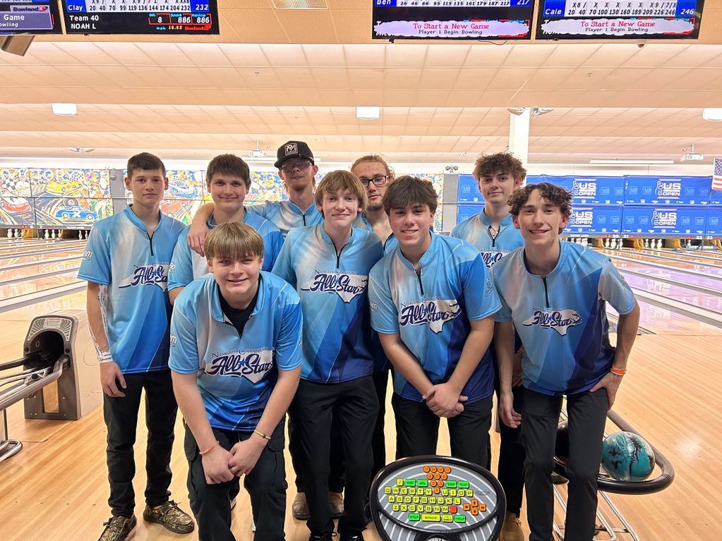 A group of young bowlers in matching blue All Stars shirts posing at a bowling alley.