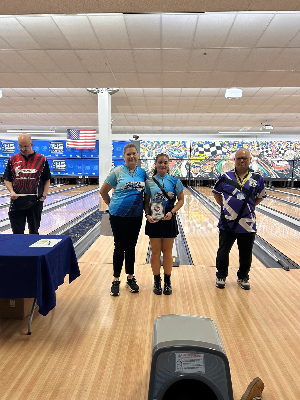 Bowling alley award ceremony with four people, one holding a plaque.