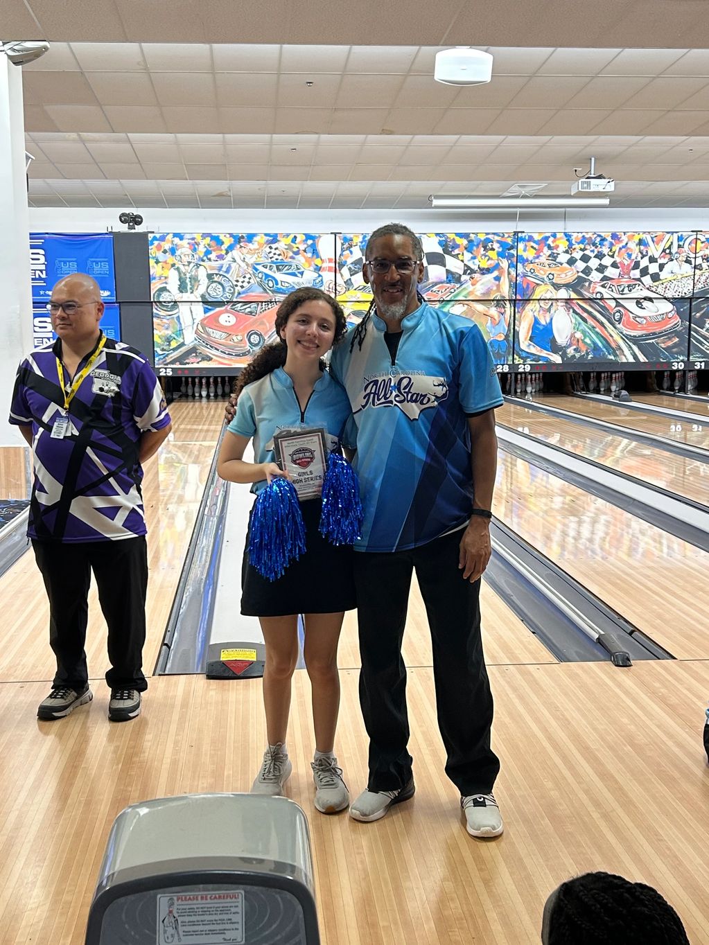 Young female bowler holding an award with coach at bowling alley.