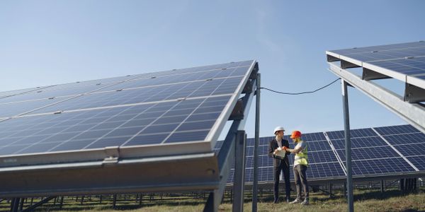 Photo of a solar farm with two workers in the background by Gustavo Fring from Pexels