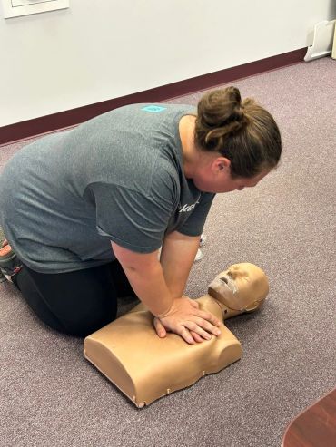 Person practicing CPR on a manikin indoors.