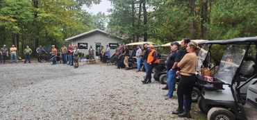 People gather outdoors near golf carts and a small building.
