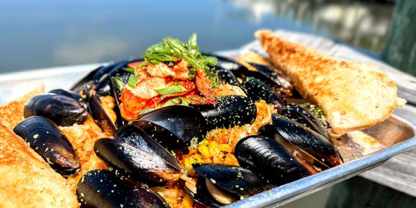 Seafood dish with mussels, shrimp, rice, and toasted bread by the water.