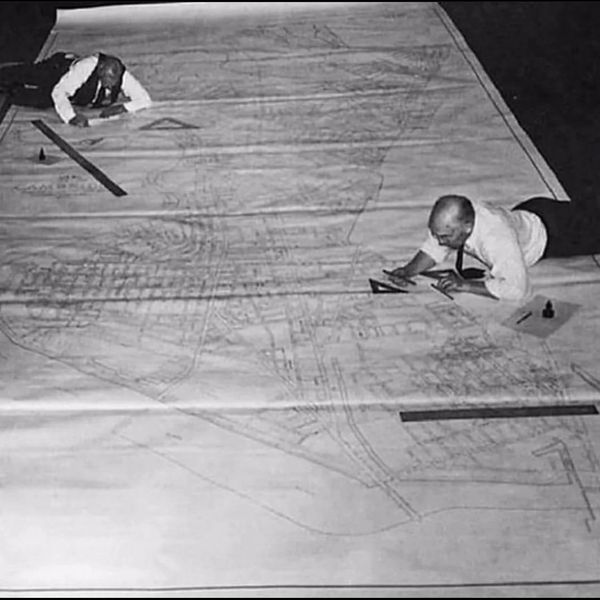 Two men working on a large architectural blueprint on the floor.