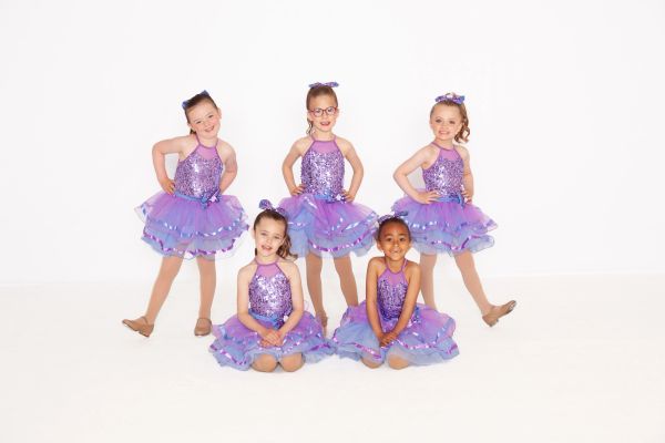 Five young girls in purple dance costumes posing for a photo.