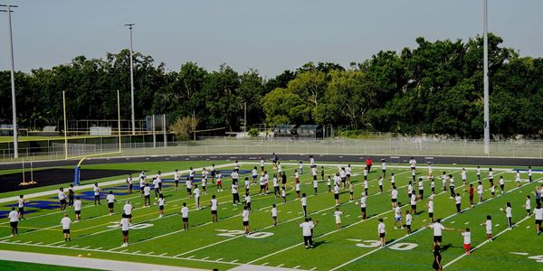Large group exercising on a football field in organized rows.
