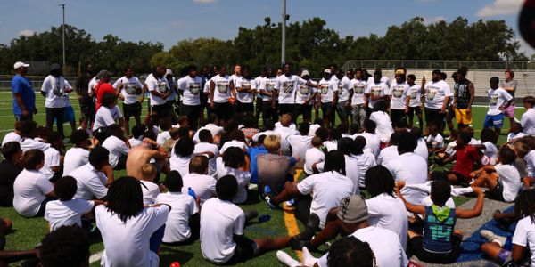 Large group of young athletes gathered on a sports field, listening to coaches.