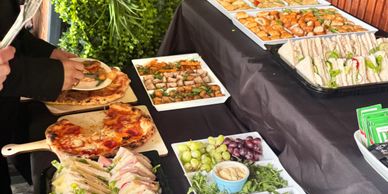 A buffet table with pizza, sandwiches, and appetizers being served.