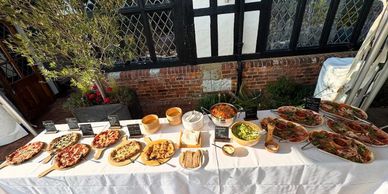 A buffet table with various pizzas and salads set outdoors against a brick wall.