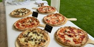 Six different pizzas displayed on wooden serving boards outdoors.
