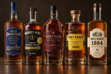 Five whiskey bottles lined up on a wooden surface.