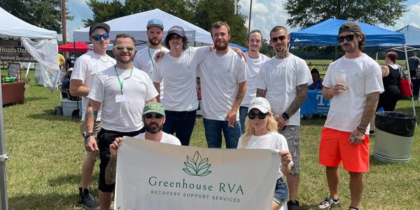 Group of people in white shirts holding a Greenhouse RVA banner outdoors.
