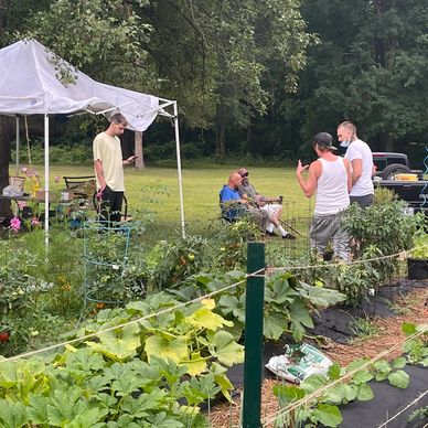 People socializing in a garden with a white canopy and lush plants.