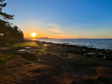 Sunset over a rocky shoreline with calm waters and clear skies.