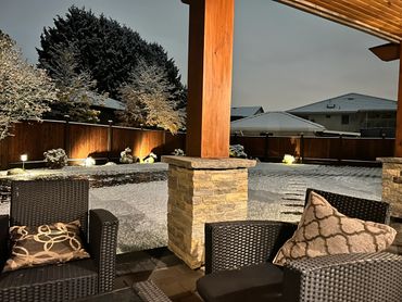 Cozy outdoor patio with cushioned chairs overlooking a snow-dusted backyard at dusk.