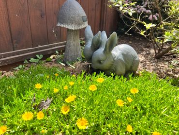 Garden scene with a bunny statue and mushroom decoration among yellow flowers.