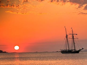 Sailboat silhouetted against a vibrant orange sunset over calm waters.