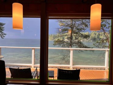 Cozy indoor view overlooking a tranquil lake with deck chairs and warm hanging lights.