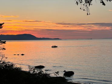 A tranquil sunset over calm waters with a boat silhouetted on the horizon.