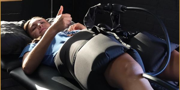 Woman lying down with a thumbs up while wearing compression therapy sleeves on her legs.
