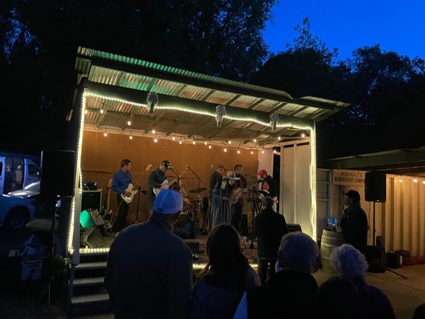 Outdoor night concert with a band performing on a small lit stage.