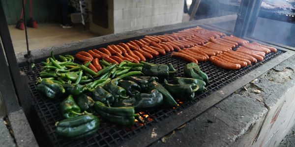 Sausages and peppers grilling on a large outdoor grill.