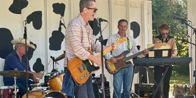 Band performing outdoors with instruments and microphones.