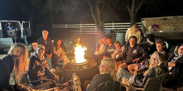 Group of friends gathered around a campfire at night outdoors.