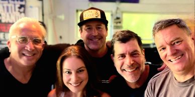 Group of five smiling friends posing for a casual photo indoors.