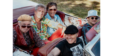 Five men in colorful outfits sitting in a vintage convertible car.