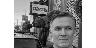 Man with a contemplative expression standing near a theater marquee.