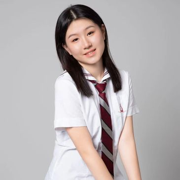 Young woman in a school uniform sitting on a stool, smiling gently.