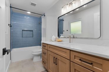 Modern bathroom with blue tile shower and wooden vanity.