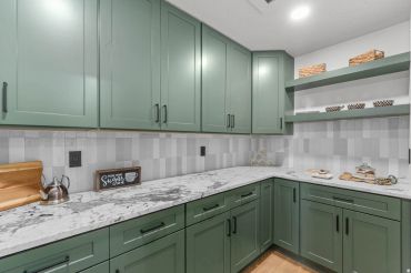Modern kitchen with green cabinets and marble countertops.