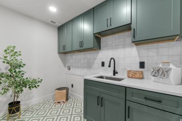 Modern laundry room with green cabinets and patterned floor.