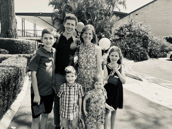 A happy family of six posing outdoors on a sunny day.