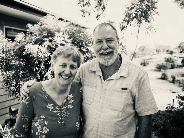 Smiling elderly couple standing outside with arm around each other.