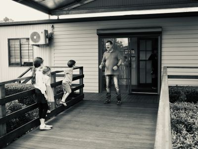 A man rollerblading towards three children on a porch.