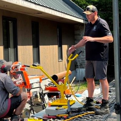 Two men working with construction equipment outside a building.