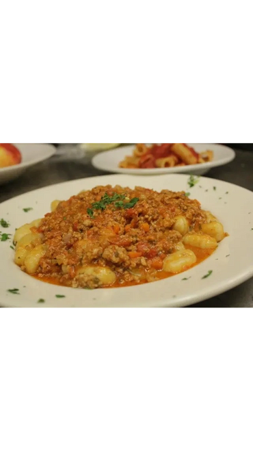 Plate of gnocchi topped with rich meat sauce and garnished with herbs.