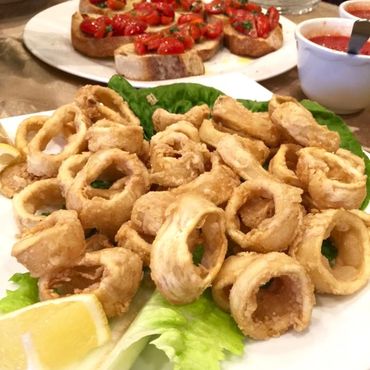 Plate of fried calamari with lemon wedges and bruschetta in the background.