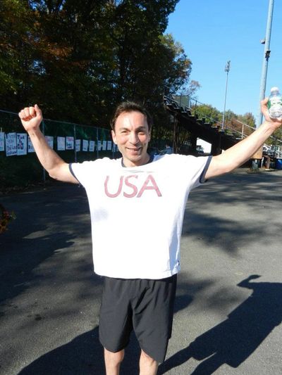 Man celebrating outdoors wearing a USA t-shirt with arms raised.